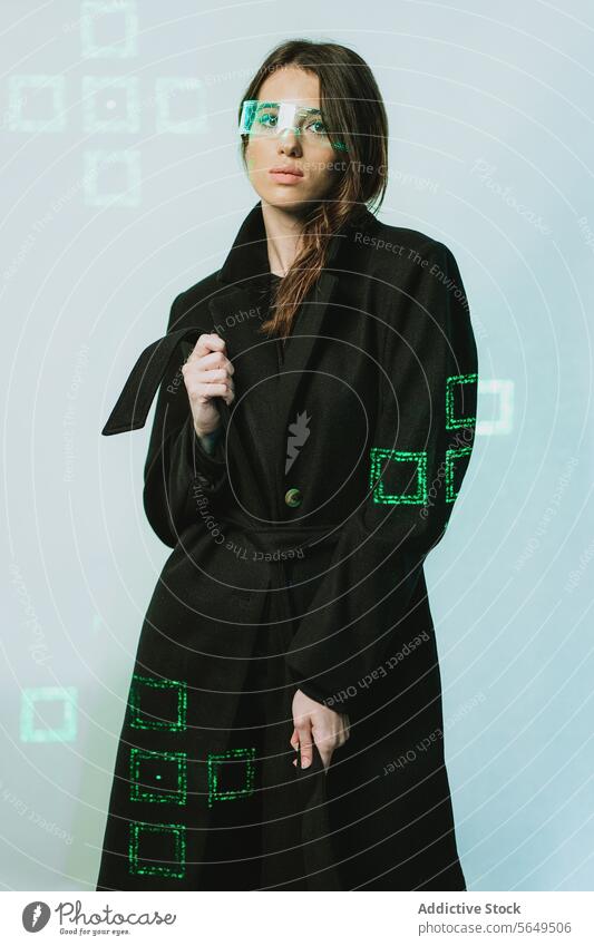 Porträt einer jungen Frau mit einer futuristischen VR-Brille und einem langen schwarzen Trenchcoat, die vor einem beleuchteten Hintergrund in die Kamera schaut