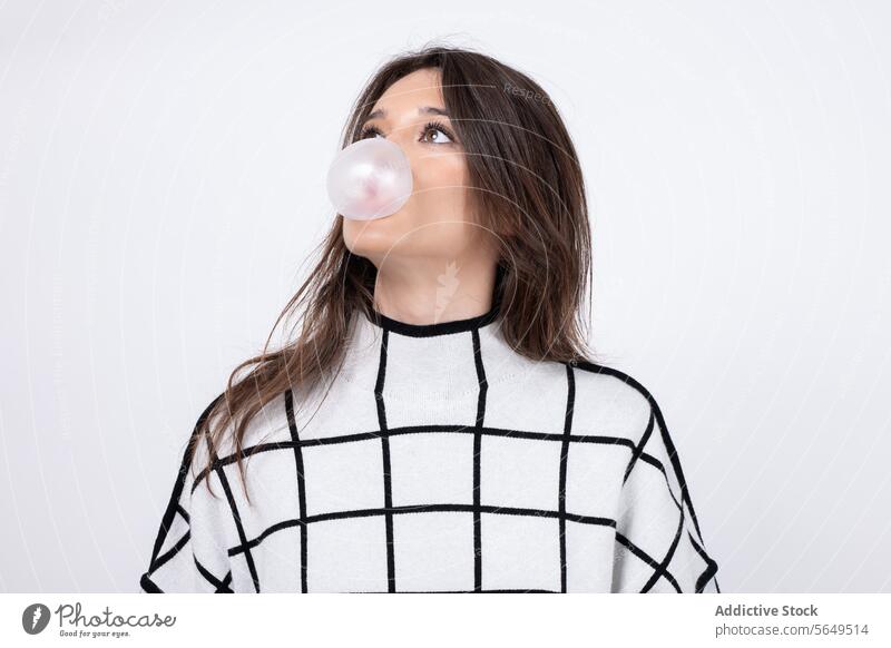 Nachdenkliche junge Frau pustet Kaugummi vor weißem Hintergrund Schlag Schaumblase Zahnfleisch nachdenklich Model Wegsehen Pullover cool hübsch vereinzelt