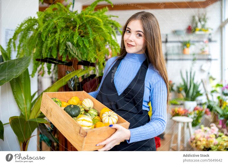 Lächelnde Frau mit einer Schachtel frischer Kürbisse in der Floristik Blumenhändler führen Arbeit Laden Kasten Glück Werkstatt Besitzer positiv Job