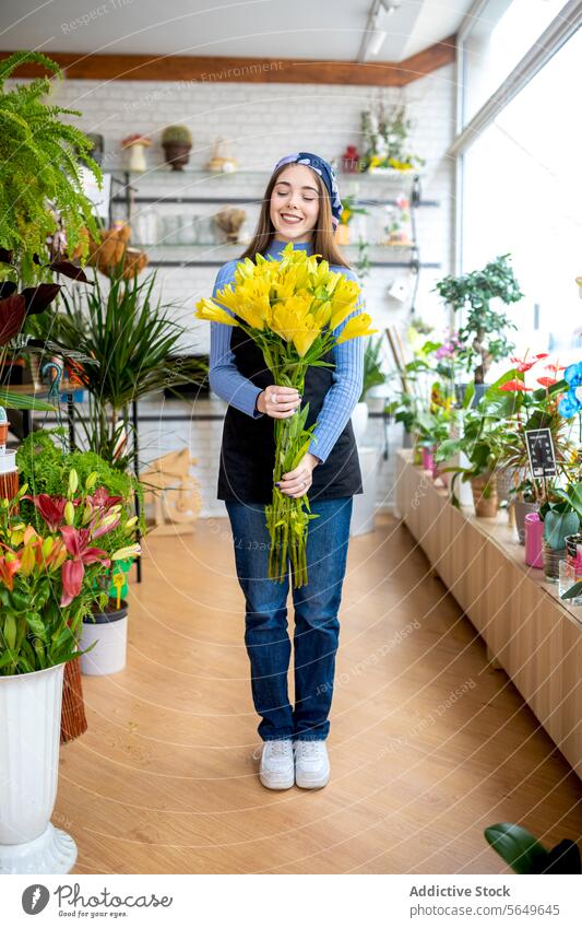 Lächelnde junge Floristin in Freizeitkleidung und Kopftuch, die frische gelbe Blumen hält, während sie tagsüber in der Floristik arbeitet Frau Blumenhändler