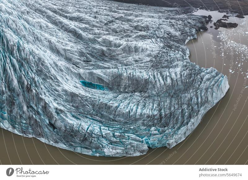 Luftaufnahme von oben, die einen Gletscher zeigt, der durch den Vatnajokull-Nationalpark in Island fließt, umgeben von zerklüftetem Gelände