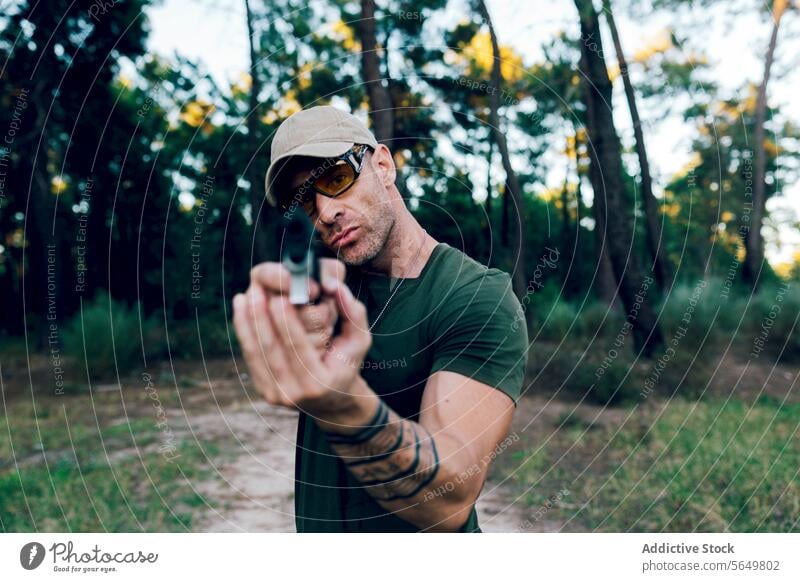 Militärsoldat, der mit einem Gewehr zielt und in die Kamera schaut, vor einem Wald Mann Kommando Pistole Waffe Armee speziell zwängen Unschärfe Soldat