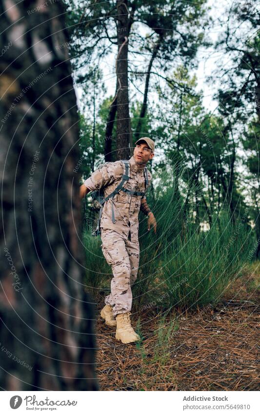 Ganzer Körper eines Armeekommandos mit Mütze und Rucksack im Wald stehend und wegschauend Mann Soldat Militär Tarnung Uniform Kommando