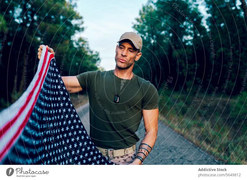 Militärsoldat, der die Nationalflagge mit Stolz hält und betrachtet, während er auf der Straße vor dem Wald steht Mann Kommando Amerikaner Fahne national
