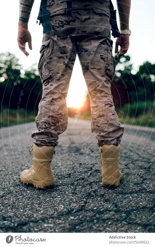 Crop Beine der anonymen Krieger stehen auf der Straße bei Sonnenuntergang Mann Kommando Tarnung Stiefel Uniform Frontlinie gesichtslos Stehen