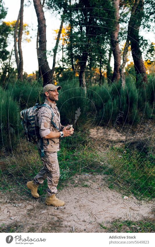 Ganzkörper-Armee-Kommando mit Mütze und Rucksack, das eine Kiste hält, die im Wald steht und wegschaut Mann Soldat Militär Tarnung Uniform Kasten