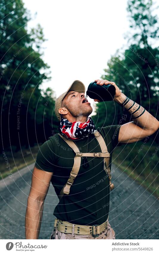 Älterer Armeesoldat trinkt Wasser, während er auf der Straße gegen den Himmel steht Mann Kommando Flasche trinken Abschrecken durstig marin Soldat grün