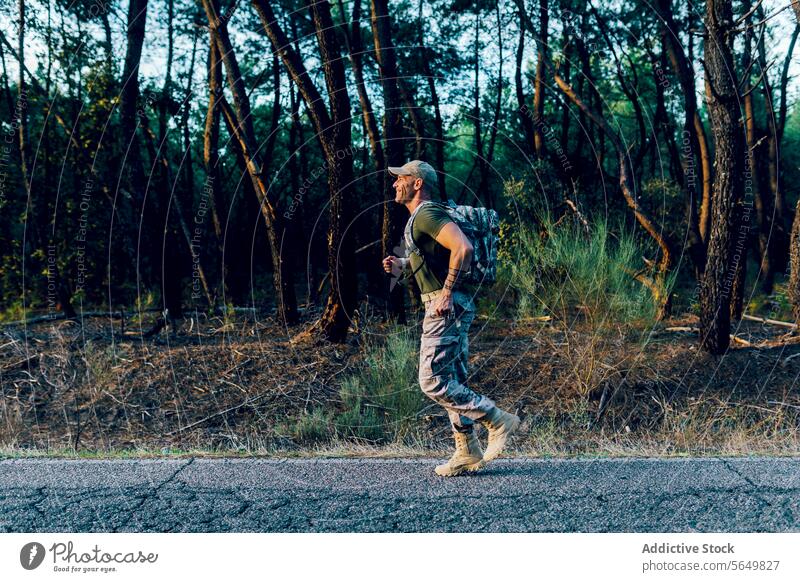 Ganzer Körper eines lächelnden Soldaten, der beim Joggen durch Pflanzen und Bäume trainiert Mann Kommando marin rennen Rucksack Straße Fitness Uniform Training