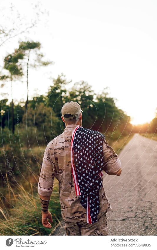 Unerkennbar Älteres Kommando auf der Straße mit amerikanischer Flagge auf der Schulter bei Sonnenuntergang Mann Soldat Amerikaner Fahne laufen Tarnung Uniform