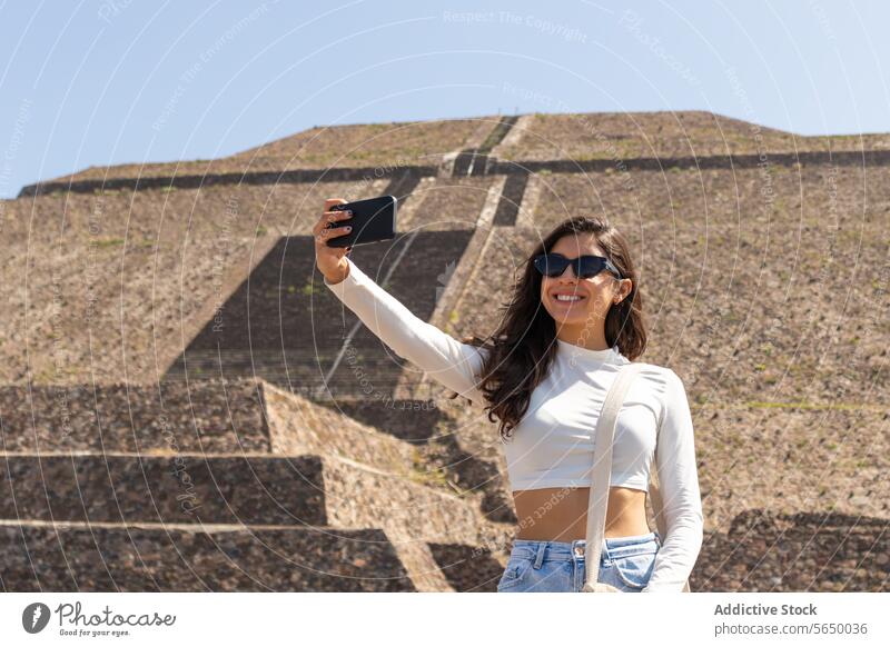 Positiv gestylter Reisender, der ein Selfie während eines Ausflugs zu einer Sehenswürdigkeit in Mexiko macht Frau Sightseeing Sonnenbrille Pyramiden Smartphone