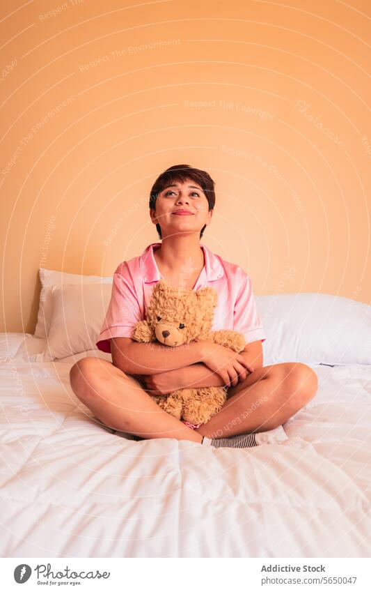 Junge Frau sitzt mit Teddybär auf dem Bett Bär Spielzeug Umarmung Lächeln Plüsch gemütlich Schlafzimmer jung Komfort Glück Pyjama Nachtwäsche