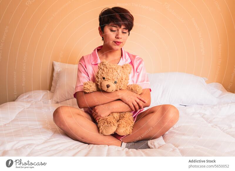 Junge Frau sitzt mit Teddybär auf dem Bett Bär Spielzeug Umarmung Plüsch gemütlich Schlafzimmer jung Komfort Pyjama Nachtwäsche sich[Akk] entspannen Dame
