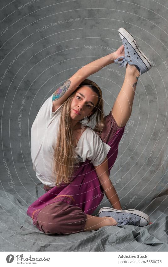 Ganzkörperdarstellung einer jungen Frau in flexibler Yogastellung, die ihr Bein nach oben streckt und in die Kamera schaut Flexibilität strecken