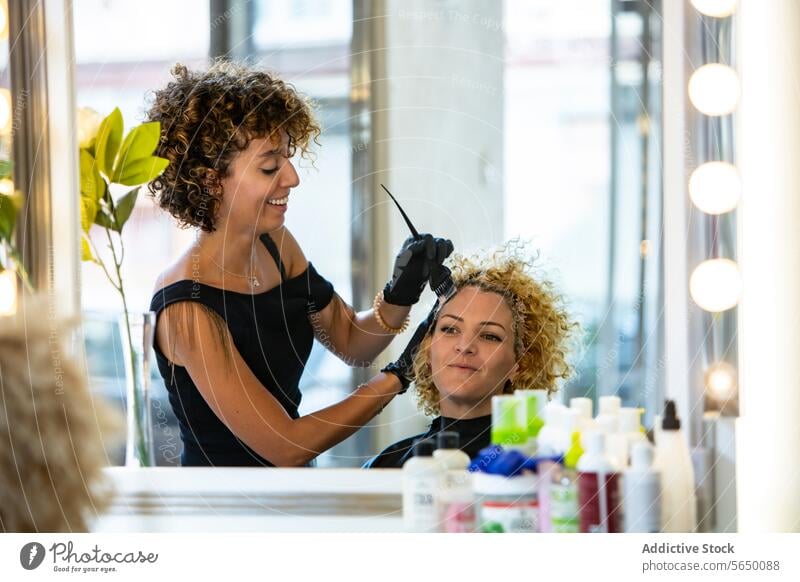 Friseurin, die in einem Salon Farbe auf das lockige Haar einer Kundin aufträgt Klient Haarfarbe krause Haare färben Haarpflege Lächeln Schönheit Pflege