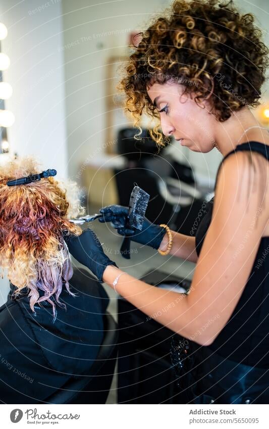Friseurin trägt im Salon Farbe auf das Haar eines Kunden auf Behaarung Klient Färbung Farbstoff Anwendung lockig Professionalität Schönheit Behandlung
