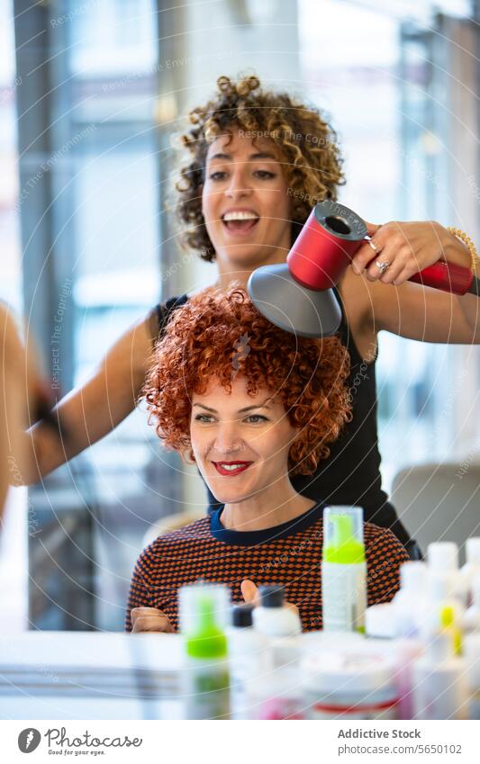 Friseurin föhnt das lockige Haar einer Kundin im Friseursalon Behaarung Stylist Salon Frau rote Haare Föhn professionell Schönheit Klient Frisur modern Lächeln