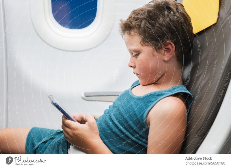 Junger Junge im Flugzeug in Tablet vertieft Kind Sitz Tablette Funktelefon Telefon Bildschirm Technik & Technologie reisen Fenster jung Passagier digital Gerät