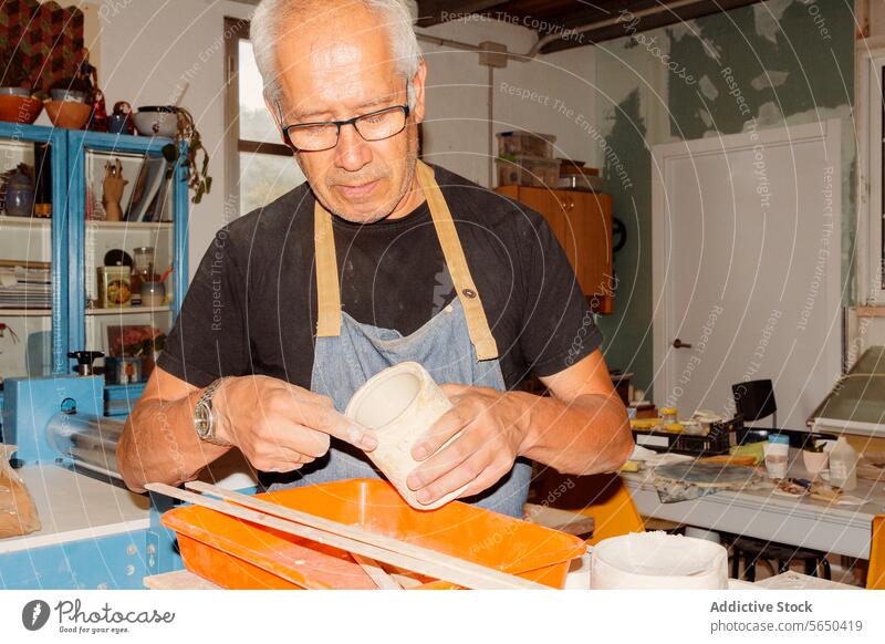 Kunsthandwerker bei der Arbeit in einer Töpferwerkstatt Kunstgewerbler Ton Vase Schaber zerkratzen Keramik Schürze Töpferwaren Werkstatt männlich stehen lässig