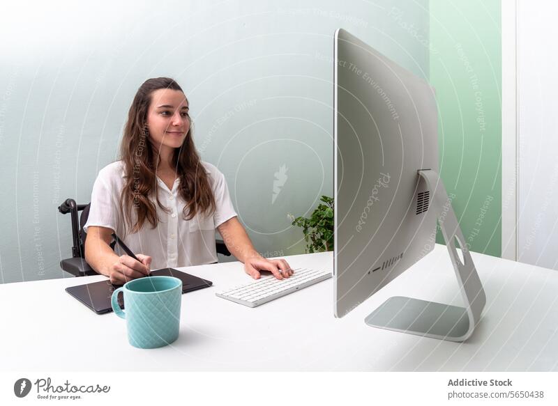 Modernes Home Office Setup mit weiblicher Fachkraft im Rollstuhl Frau Büro heimwärts Computer Desktop Tablette Becher Arbeit professionell modern elegant Design