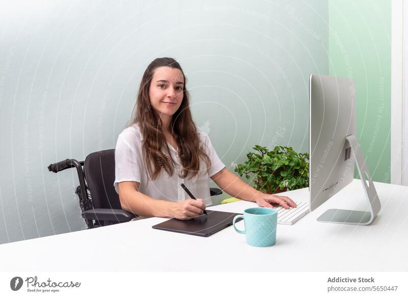 Professionelle Frau arbeitet im Rollstuhl an einem modernen Schreibtisch professionell Computer digitales Tablett Büro Arbeit fokussiert Sauberkeit