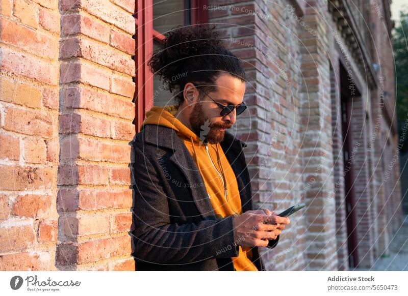 Stilvoller Mann mit Smartphone in städtischer Umgebung urban Straße Sonnenuntergang Mode Großstadt jung Erwachsener männlich krause Haare Haarknoten Texten
