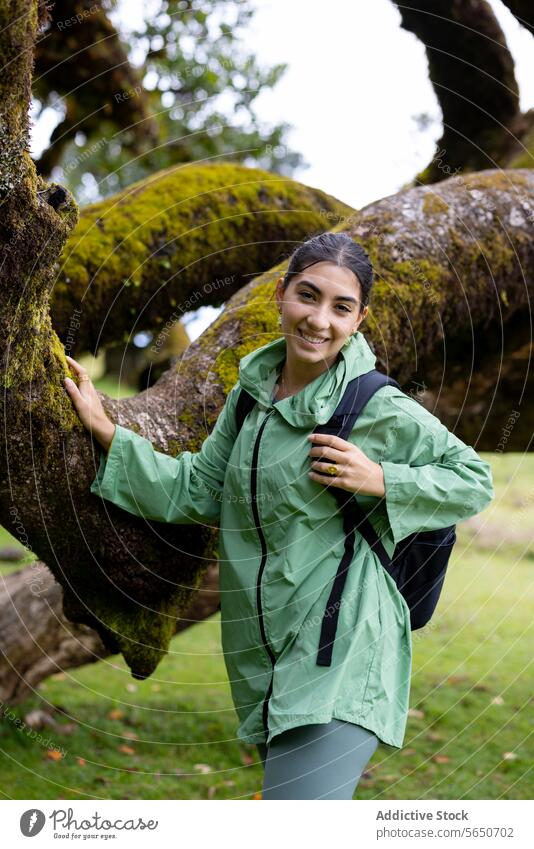 Lächelnde Wanderin im Wald mit unscharfem Hintergrund Frau wandern Regenmantel Baum Glück Moos Rucksack grün Stehen deckend Wanderer Abenteuer