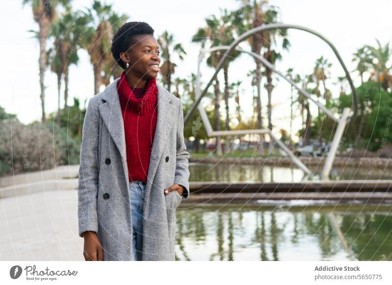 Lächelnde schwarze Frau in der Nähe eines Teiches im Park Großstadt Hafengebiet Wasser Oberbekleidung Wochenende Herbst Freizeit laufen positiv Glück genießen
