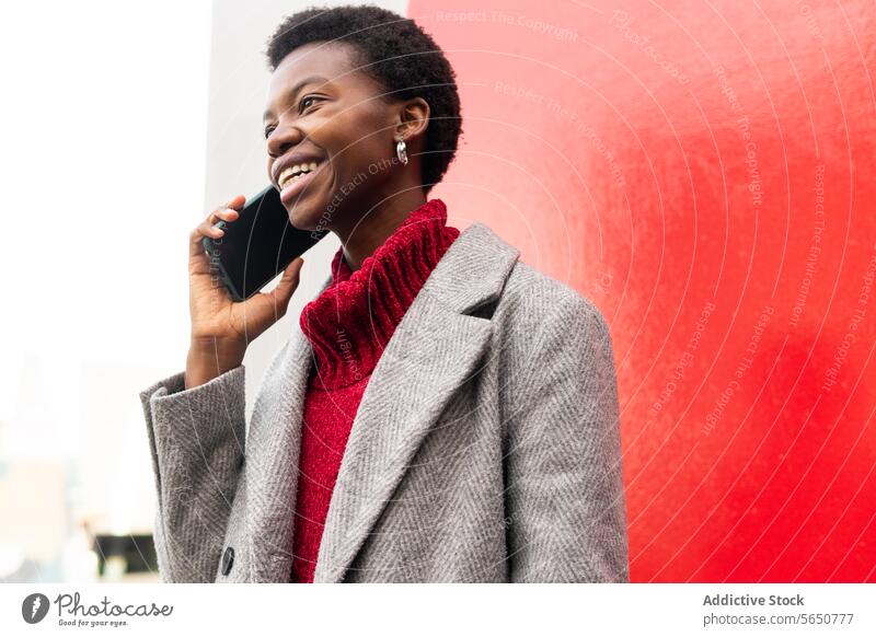 Fröhliche afroamerikanische Frau, die auf der Straße mit ihrem Smartphone spricht Telefonanruf Funktelefon benutzend sprechen reden Kommunizieren Talkrunde Stil