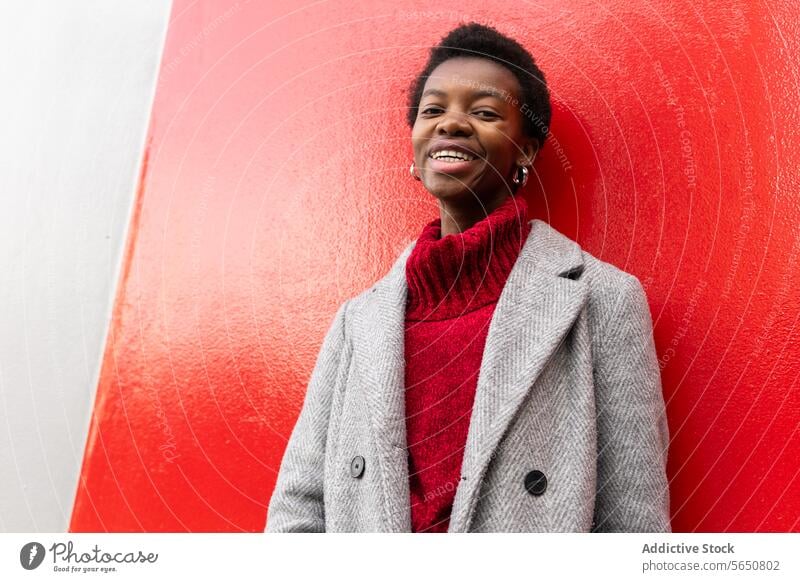 Afroamerikanische Frau steht in der Nähe des Gebäudes rote Wand Stil Jacke Straße Individualität Vorschein Persönlichkeit Pullover Porträt schwarz stehen