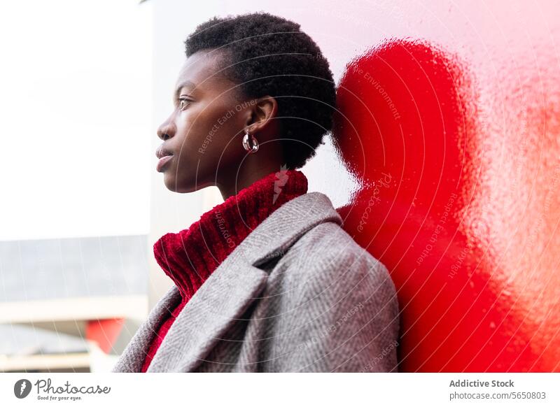 Afroamerikanische Frau steht in der Nähe des Gebäudes rote Wand Stil Jacke Straße Individualität Vorschein Persönlichkeit Pullover Porträt schwarz Dame stehen