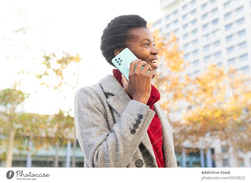 Lächelnde afroamerikanische Frau, die auf der Straße mit ihrem Smartphone spricht reden benutzend Funktelefon sprechen Großstadt Handy Surfen Glück modern