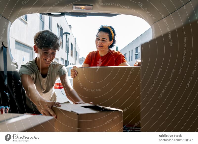 Lächelnde Mutter und Sohn, die während eines Umzugs Kisten aus dem Auto holen abholen Karton Kasten einziehen PKW Kofferraum verlegen Zugehörigkeit Schachtel