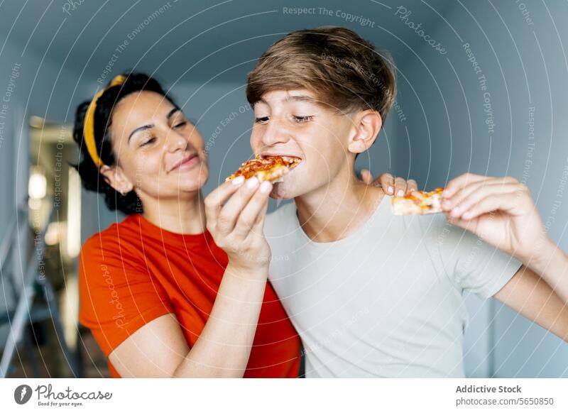 Glückliche Mutter füttert Sohn mit Pizza Mama Futter Inhalt Frieden verlegen essen heimwärts Zusammensein Liebe Lebensmittel Lächeln im Innenbereich hungrig