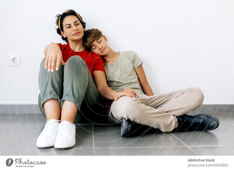 Teenager, der mit seiner Mutter auf dem Boden sitzt und den Kopf an die Schulter der Mutter lehnt Sohn sitzen Stock fettarm ruhen verlegen neu Haus Eltern