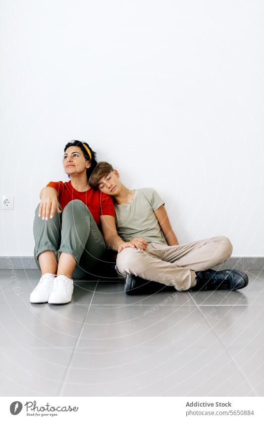 Teenager, der mit seiner Mutter auf dem Boden sitzt und den Kopf an die Schulter der Mutter lehnt Sohn sitzen Stock fettarm ruhen verlegen neu Haus Eltern