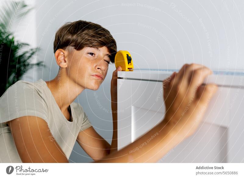Junger Teenager misst Regal mit gelbem Maßband messen nehmen Messung Kabinett Fokus Gerät benutzend modern Konzentration Werkzeug heimwärts im Innenbereich