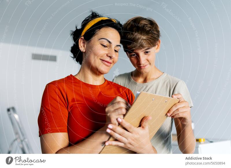 Mutter und Sohn prüfen gemeinsam Notizen auf dem Klemmbrett und lächeln Hinweis Zwischenablage diskutieren lesen Detailaufnahme Lächeln Frau Zusammensein heiter