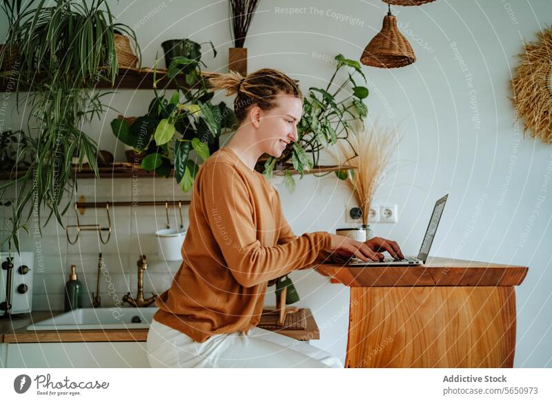 Glückliche junge Frau arbeitet am Laptop am Küchentisch mit Kaffeetasse im Tageslicht Kabinett Tisch zu Hause Rastalocken Apparatur Gerät online Netbook Browsen