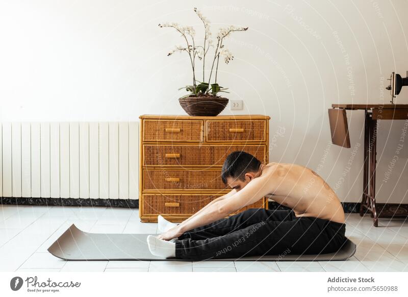 Konzentrierter junger Mann sitzt auf einer Matte und dehnt die Beine beim Training zu Hause Dehnung Rehabilitation heimwärts üben Yoga meditieren Sitzung