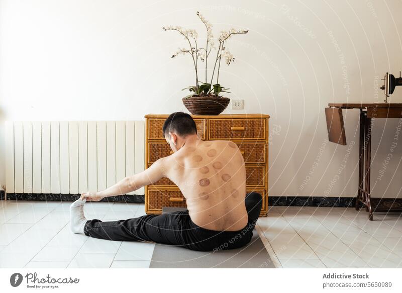 Konzentrierter junger Mann sitzt auf einer Matte und streckt sein Bein beim Training zu Hause Dehnung Rehabilitation heimwärts üben Yoga meditieren Sitzung