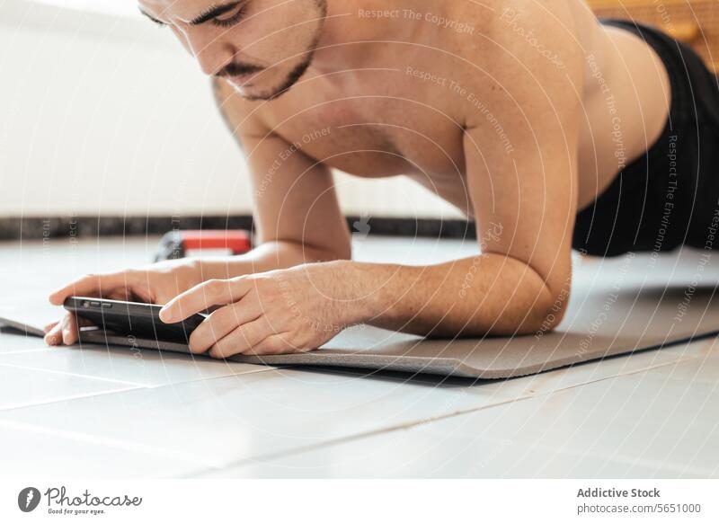 Crop-Mann während einer Rehabilitationsübung beim Surfen auf dem Smartphone Übung Textnachricht online benutzend lesen ohne Hemd Training zu Hause männlich jung
