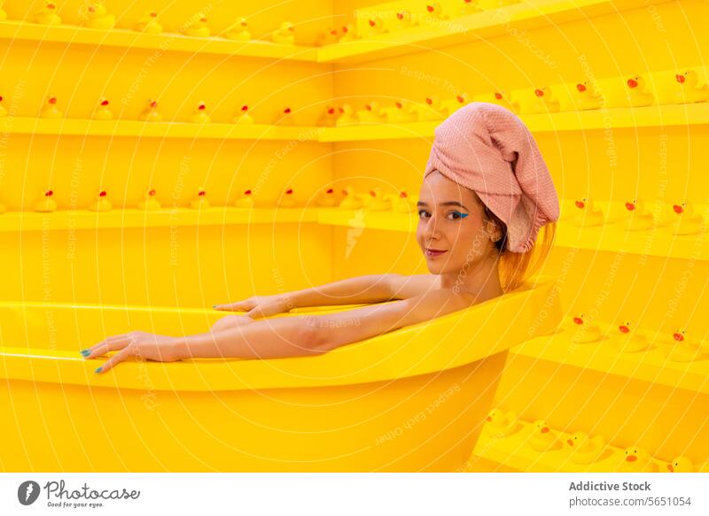 Frau entspannt sich in der Badewanne und schaut in die Kamera Handtuch Kopfverpackung entspannend gelb Gummiente monochromatisch Freizeit Selbstfürsorge