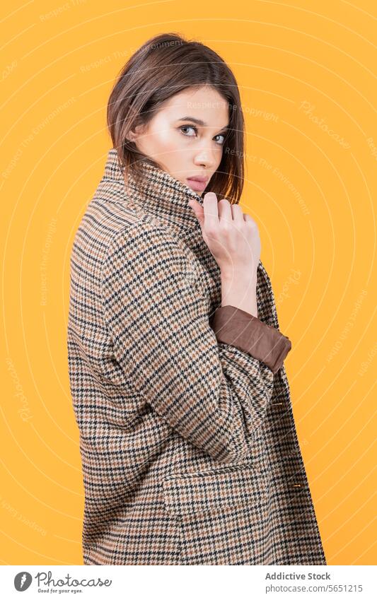 Modische Frau in modischem Mantel isoliert auf gelbem Hintergrund attraktiv langes Fell geprüft Muster Stehen in die Kamera schauen selbstbewusst trendy Eleganz