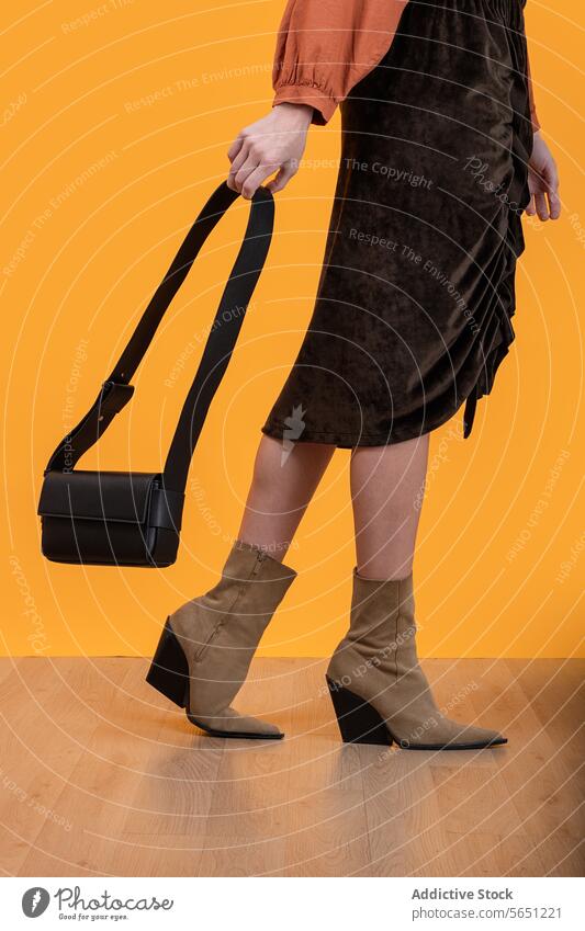 Trendige Frau in Stiefeln hält Handtasche auf dem Boden modisch Damenschuhe Geldbörse laufen Hartholz Stock gelber Hintergrund trendy Beteiligung Ernte Eleganz