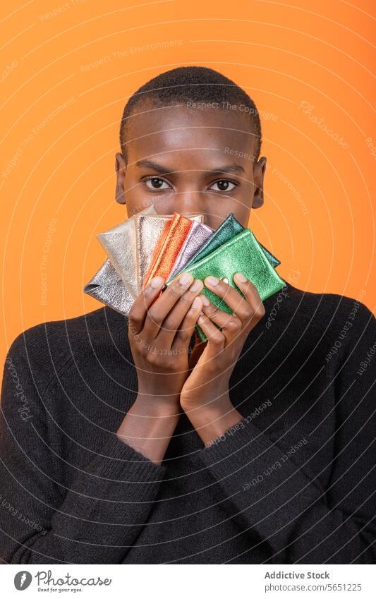 Schwarze Frau mit bunten Brieftaschen isoliert auf orangefarbenem Hintergrund mehrfarbig glänzend Afroamerikaner Beteiligung Porträt Kurze Haare vereinzelt Geld
