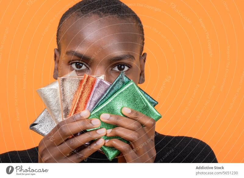 Schwarze Frau mit bunten Brieftaschen isoliert auf orangefarbenem Hintergrund mehrfarbig glänzend Afroamerikaner Beteiligung Porträt Kurze Haare vereinzelt Geld