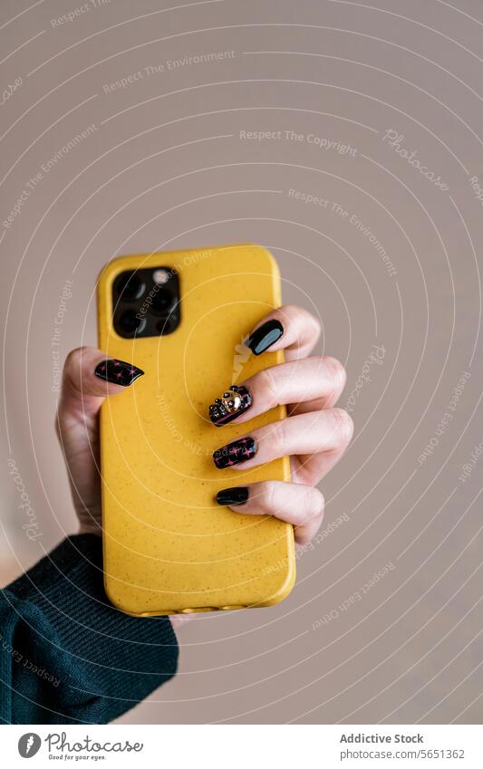 Crop Frau mit schwarzer Nagelkunst hält Handy Smartphone Maniküre Nagellack nageln Kunst kreativ gelb Stil Gerät Apparatur modern Mobile Farbe Telefon