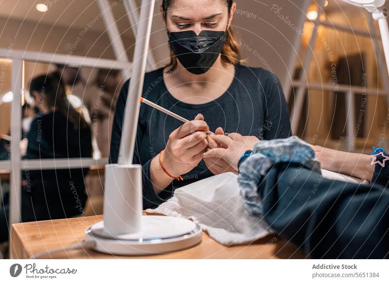 Fokussierte junge Kosmetikerin mit Maske bei der Maniküre in einem Schönheitssalon Frauen nageln professionell Salon Mundschutz Klient Arbeit Kollege Pandemie