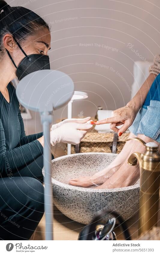 Crop-Frau bei einer Schönheitsbehandlung im Salon Frauen Maniküre Pediküre Fußbad bewerben Nagellack Kosmetikerin Leckerbissen Klient nageln Mundschutz Pflege
