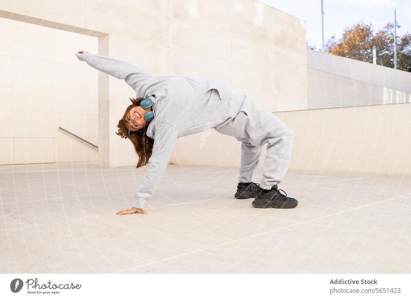 Urbaner Straßentänzer in Freizeitkleidung bei einem Auftritt im Freien Straßentänzerin urban dynamische Pose Flexibilität Stil Kopfhörer Leistung Tanzen
